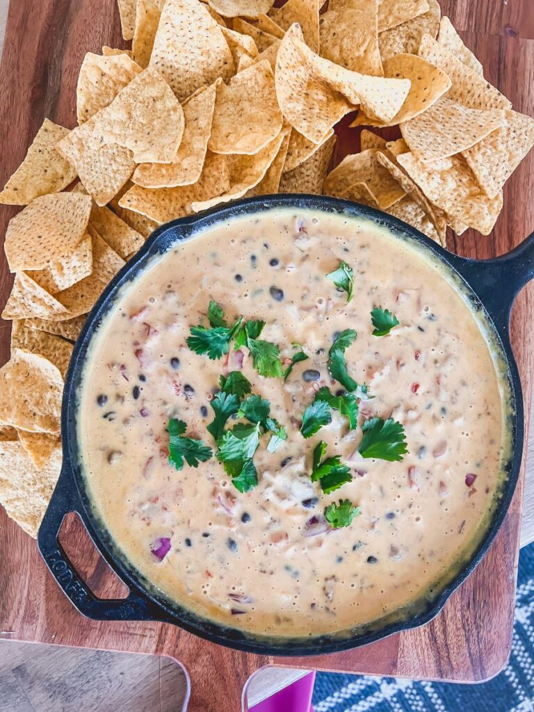 Loaded Queso Beer Dip on a wooden platter surrounded by chips