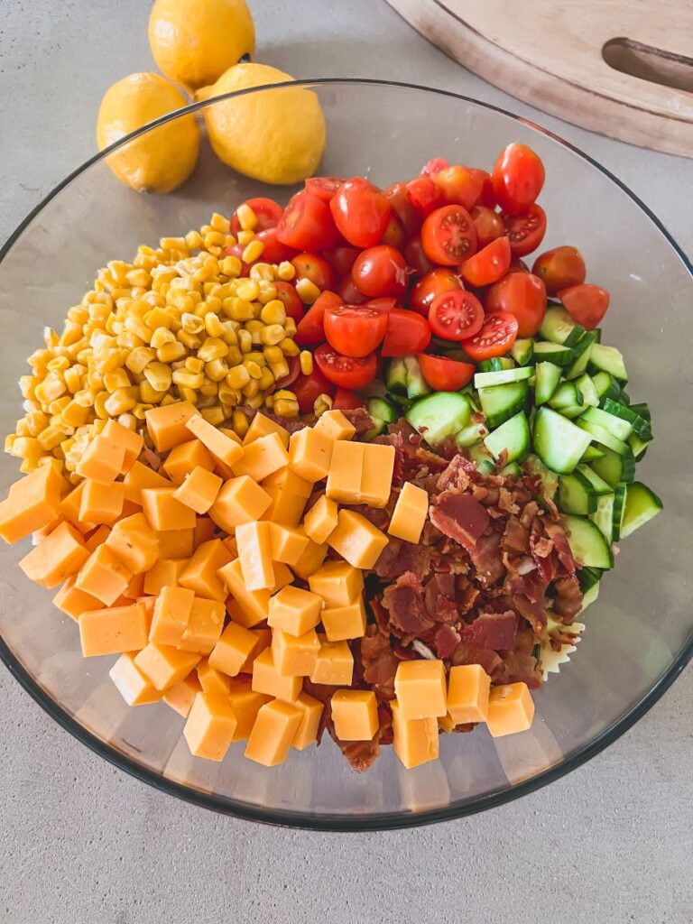 Cheese, veggies, tomatoes, and other ingredients in a clear glass bowl