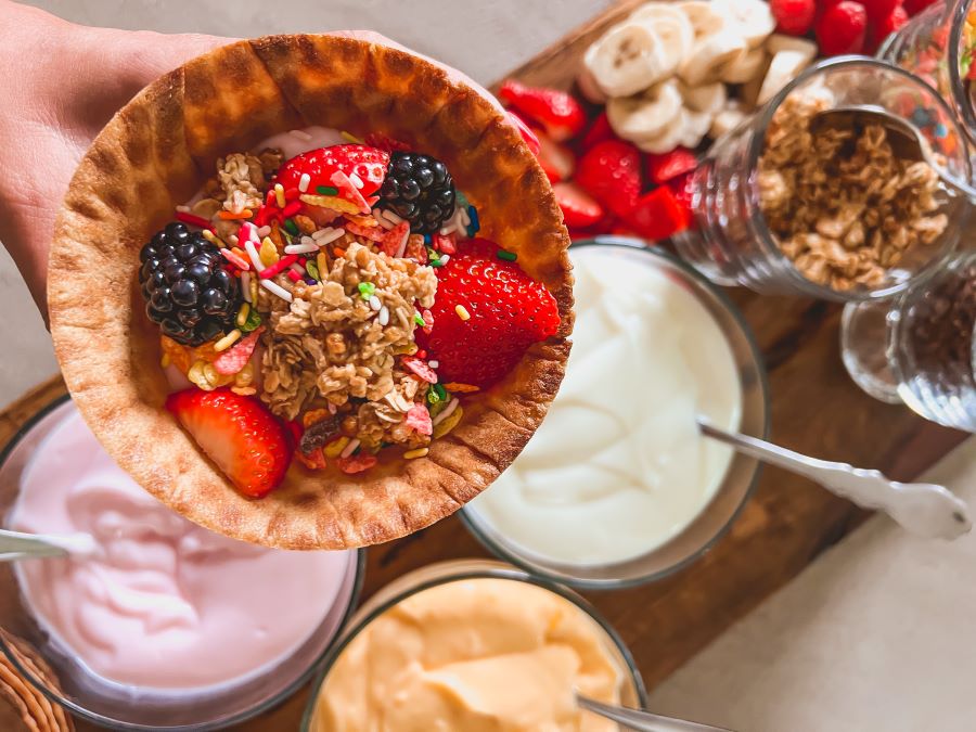 Waffle bowl filled with fruit in front of yogurt and other toppings