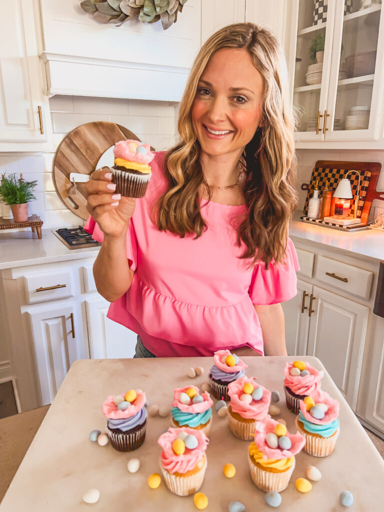 Leanna holding festive Easter cupcakes in a sunny kitchen
