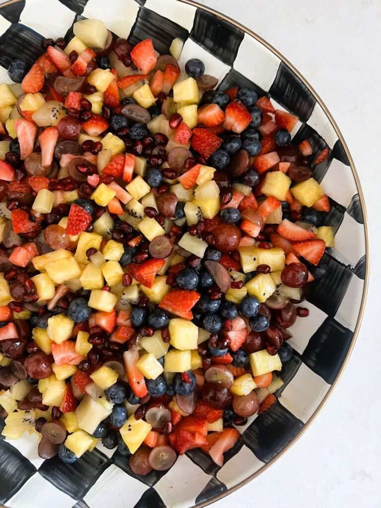 Delicious fruit salad coated in honey-lime dressing in a black-and-white checkered bowl