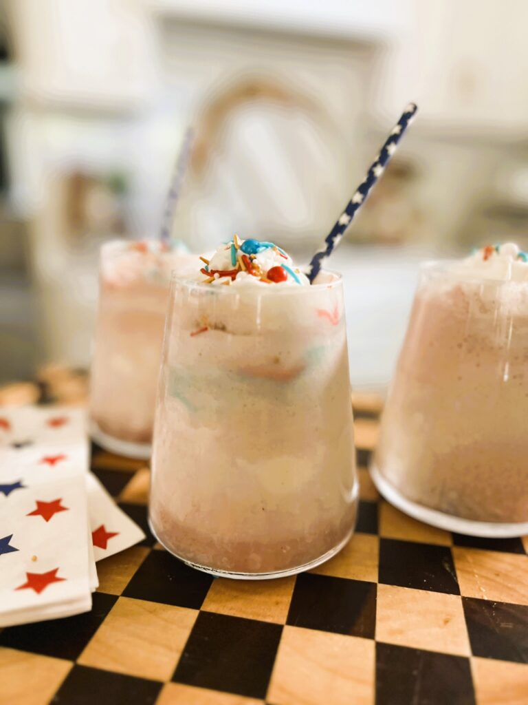 Red Wine Floats on a checkered serving board, topped with a blue straw and whipped cream