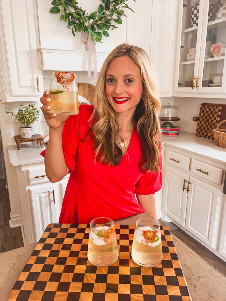 Leanna holding a Spicy Sauvignon Blanc Spritz in a sunny white kitchen