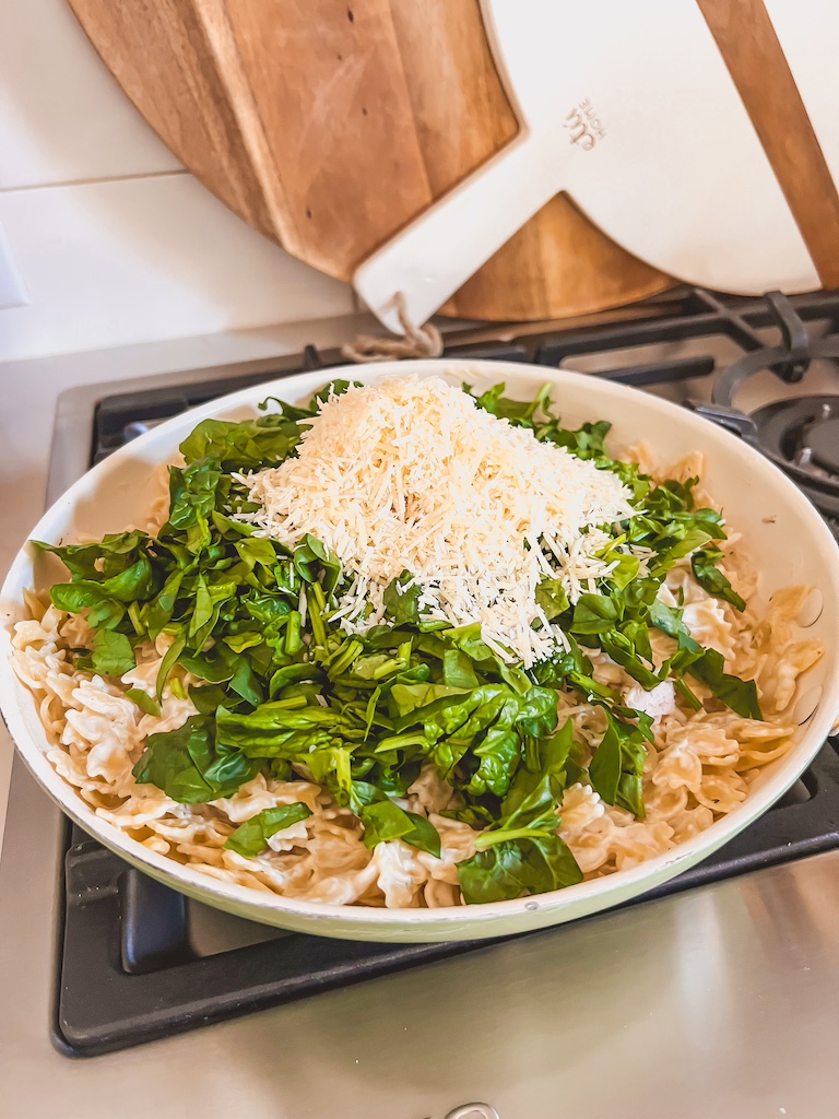 Fresh spinach being stirred into creamy Boursin chicken pasta in one pan.