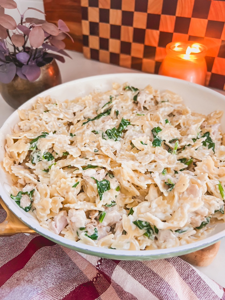 Serving creamy Boursin chicken pasta with spinach from skillet to plate.