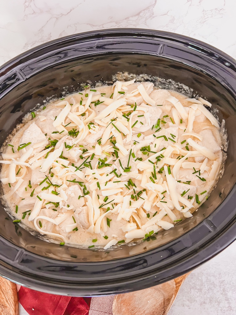 Shredded mozzarella cheese sprinkled over biscuit dumplings in the crockpot.