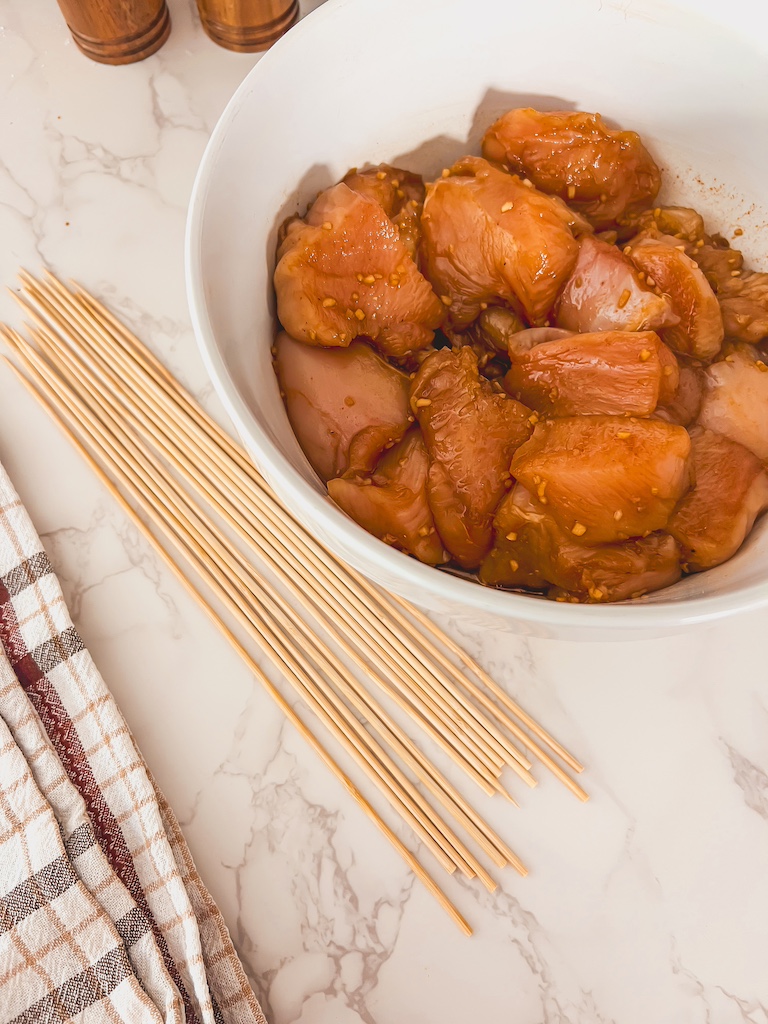 Seasoned chicken pieces being threaded onto wooden skewers before grilling