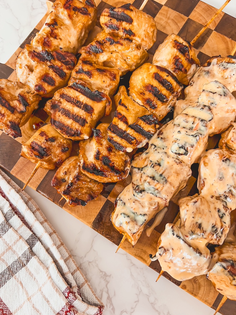 Warm chicken skewers on a plate being drizzled with creamy bang bang sauce