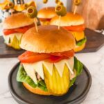 Halloween monster burger with olive eyes, pickle tongue, and cheesy teeth.