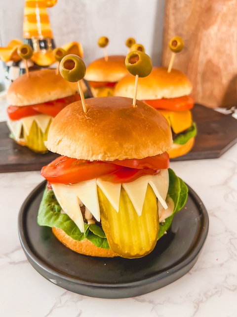 Halloween monster burger with olive eyes, pickle tongue, and cheesy teeth.