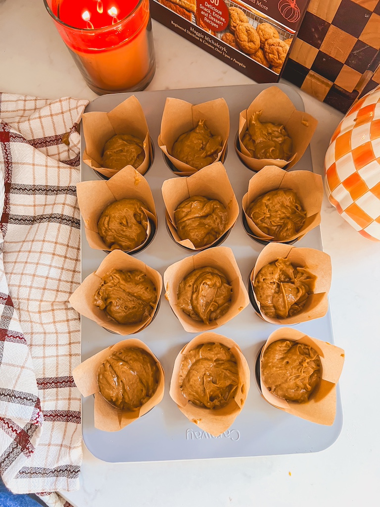 Muffin liners half-filled with pumpkin batter in a muffin tin, ready for cream cheese filling.