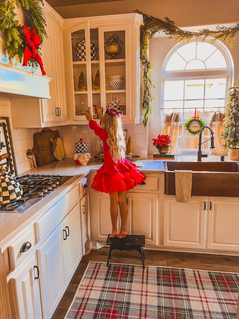 little girl in red dress pulling a mug down in a festive christmas kitchen