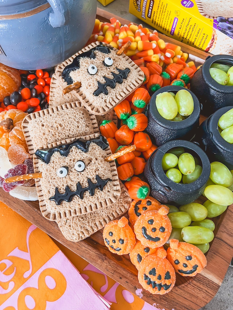 Spooky-cute Halloween snack board filled with pumpkins, grapes, and chocolate treats.