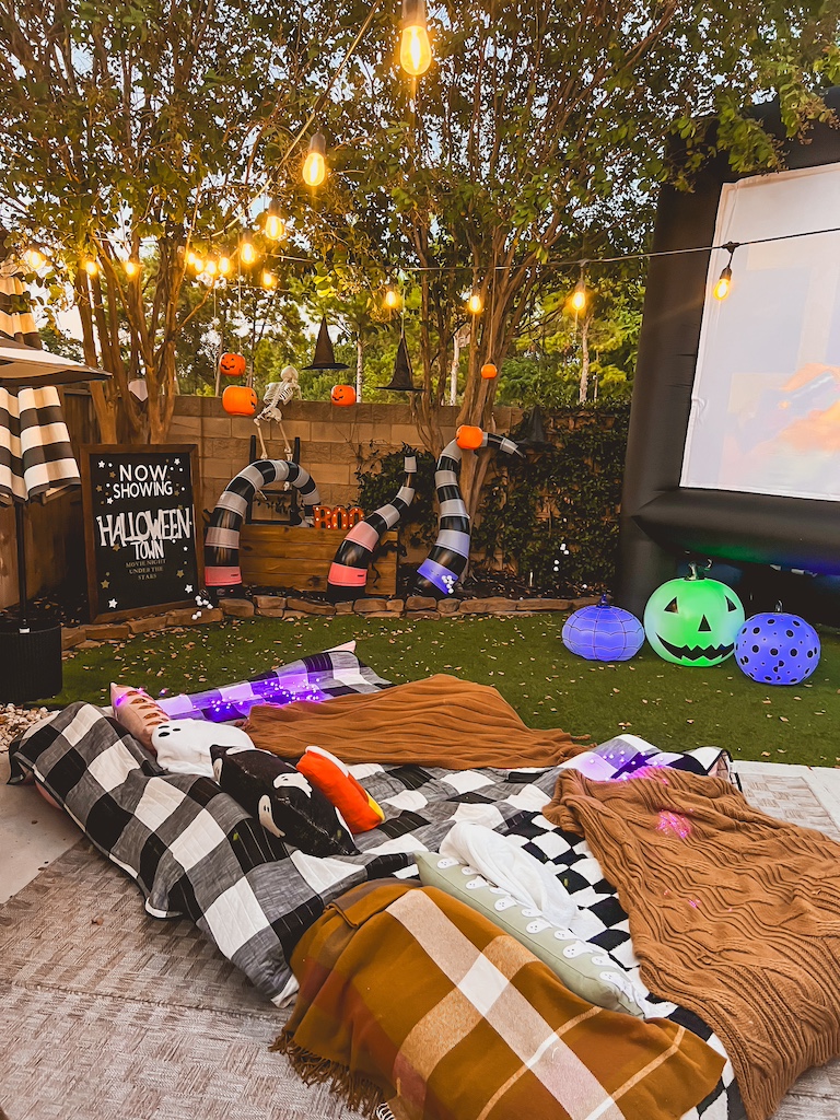 Outdoor Halloween movie night setup with hanging pumpkin buckets, witch hats, and glowing lights