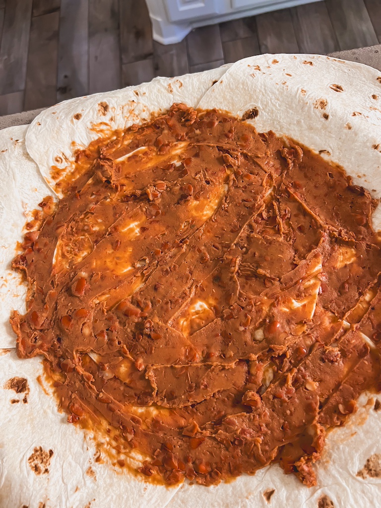Spreading refried beans evenly across tortilla base for Halloween quesadilla bake