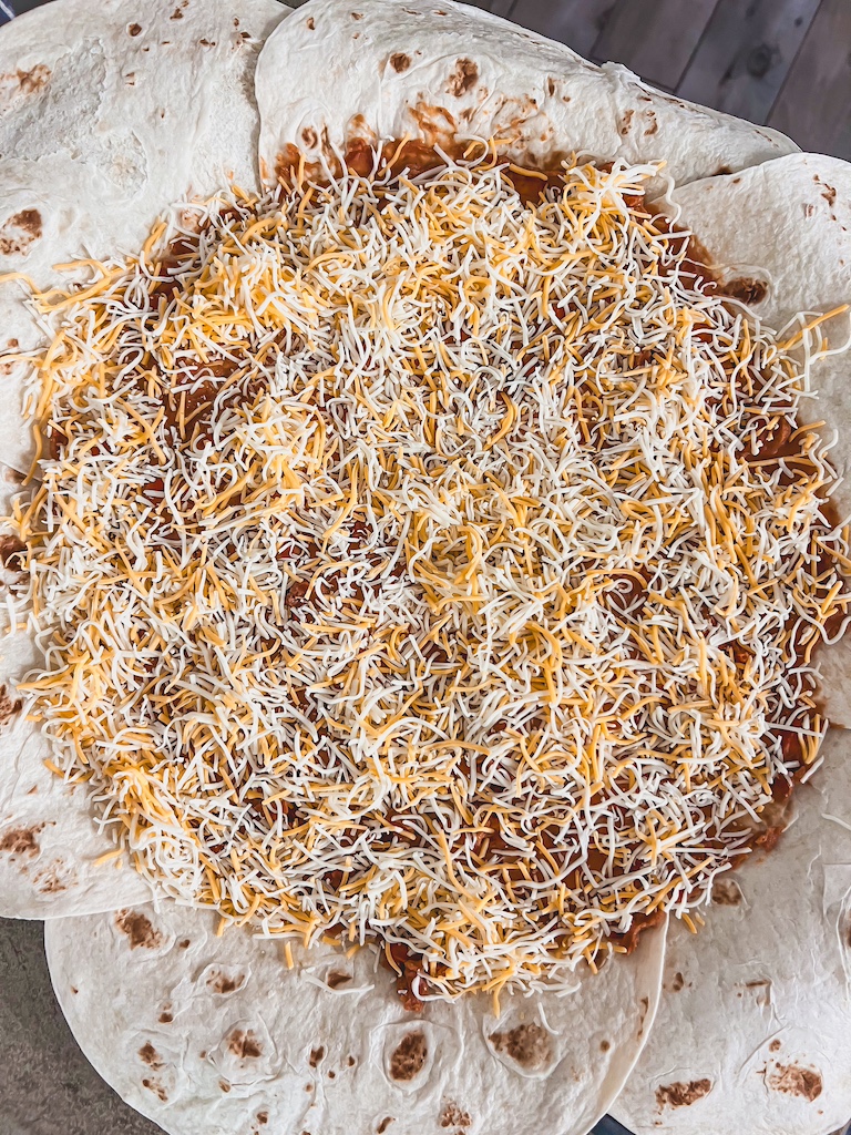 Sprinkling Kraft Mexican Blend Cheese on refried beans for cheesy Halloween quesadilla