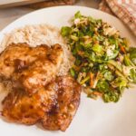 plated honey garlic chicken on white plate along side a salad and rice