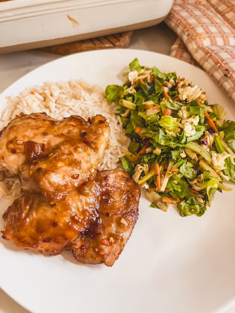 plated honey garlic chicken on white plate along side a salad and rice