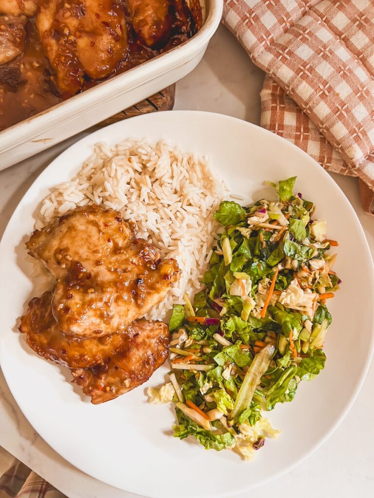 plated honey garlic chicken thighs with side salad and rice