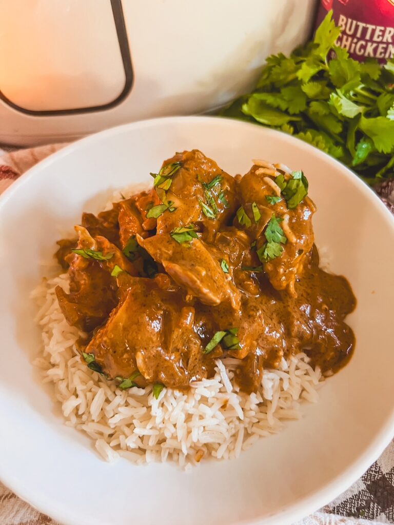 butter chicken plated in a white bowl on top of basmati rice