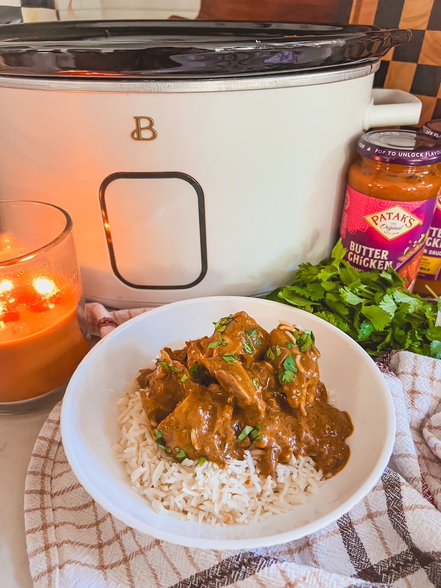 slow cooker butter chicken plated in a bowl with rice next to slow cooker and a candle