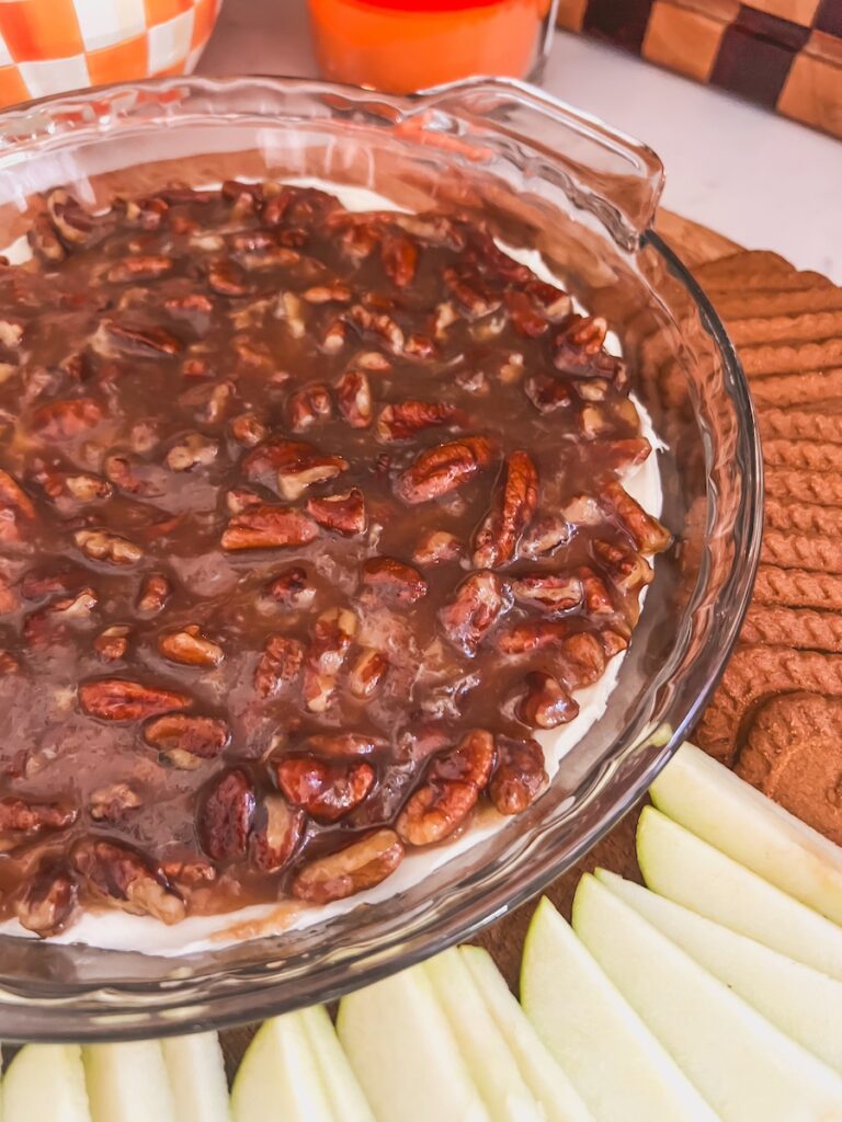 close up of pecan pie dip in glass pie dish with cookies and apples
