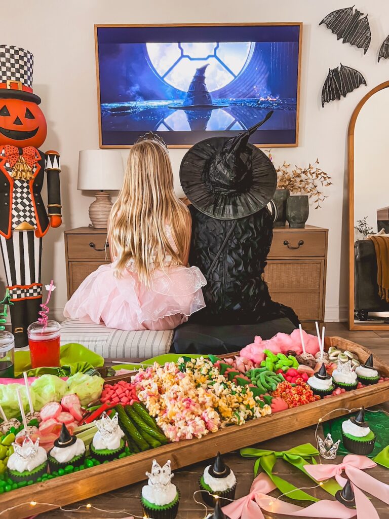 alphaba and glenda dressed up costumes watching the wicked movie with the board on the table