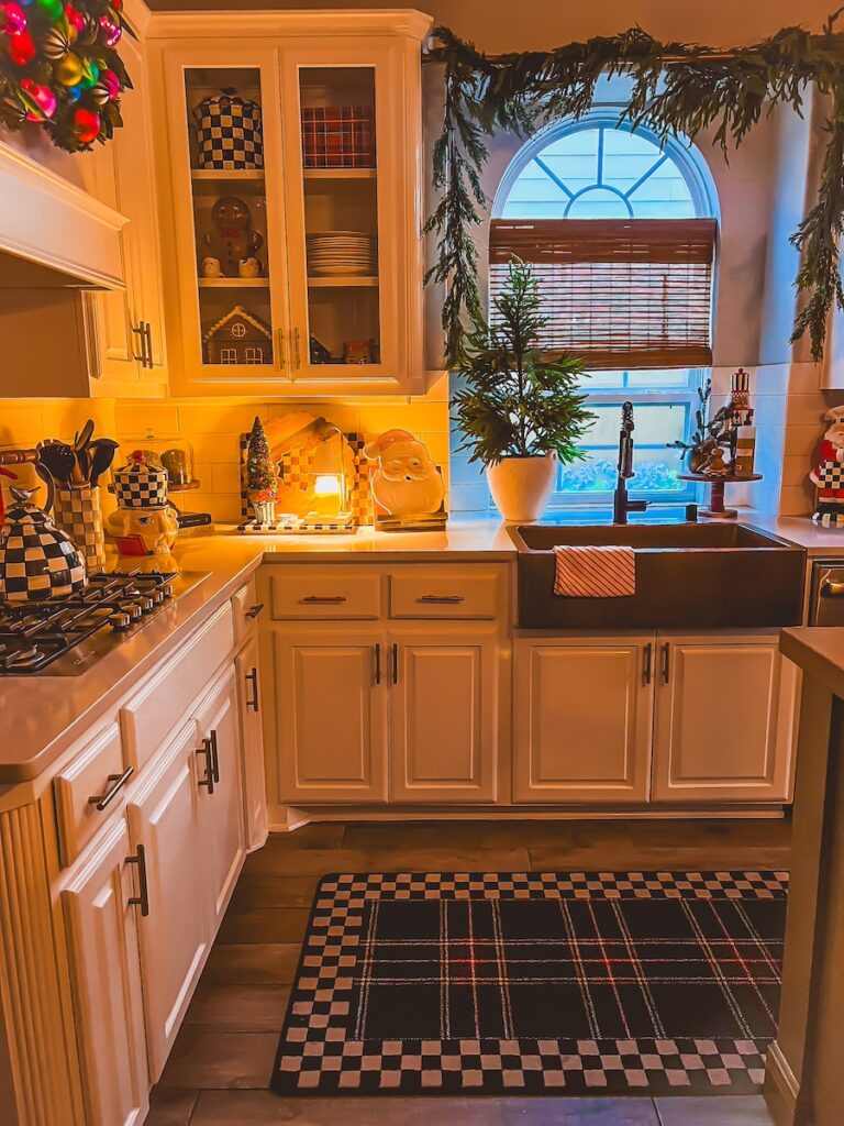 nightime view of cozy christmas kitchen with tartan plaid runner and garland hanging above the sink
