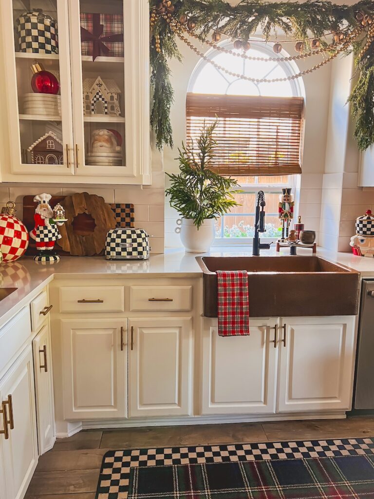 cozy christmas kitchen with white cabinets and christmas plaid with garland hanging over the sink