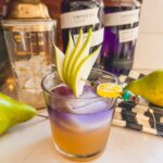 layered fall cocktail with empress gin, in a clear glass with pear garnish