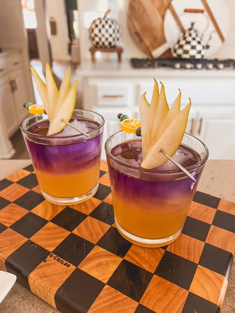 two glasses of layered fall cocktail on wood serving board