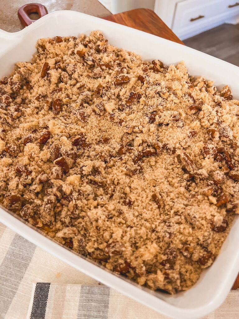 pecan crumb topping sprinkled on top of sweet potato casserole in white baking dish