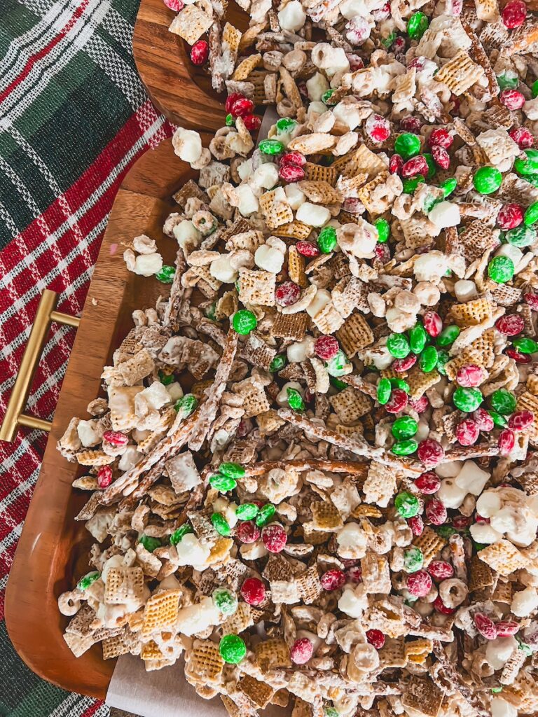 christmas crack chex mix spread out on parchment paper on top of wood board