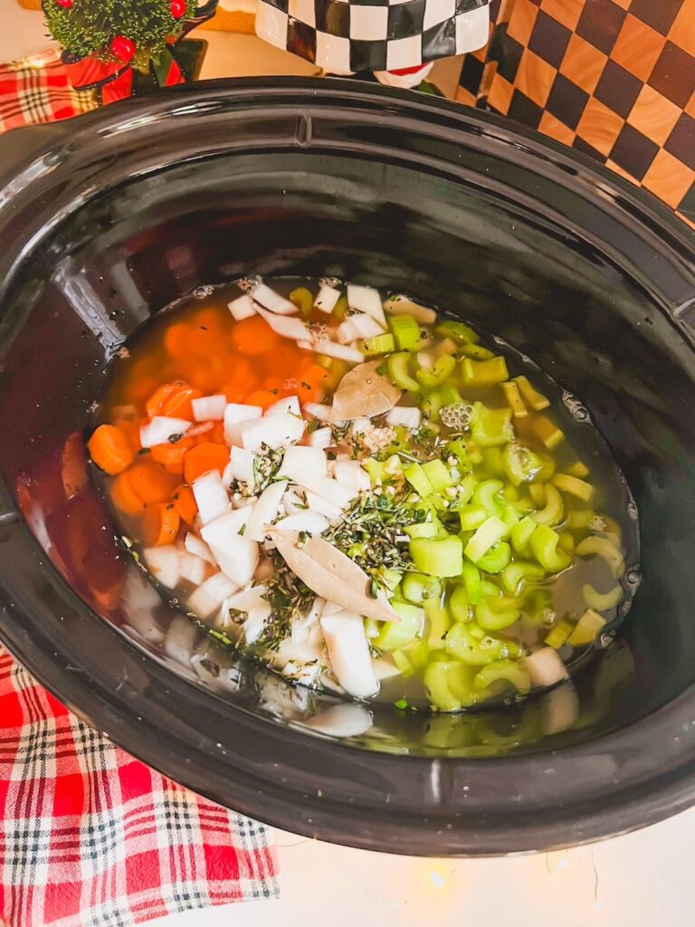 Chicken, vegetables, herbs, and broth in a slow cooker for chicken noodle soup.