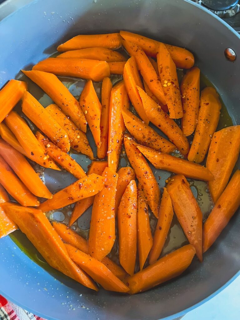 Maple glazed carrots cooking in a skillet with oil, butter, maple syrup, and chili flakes. 