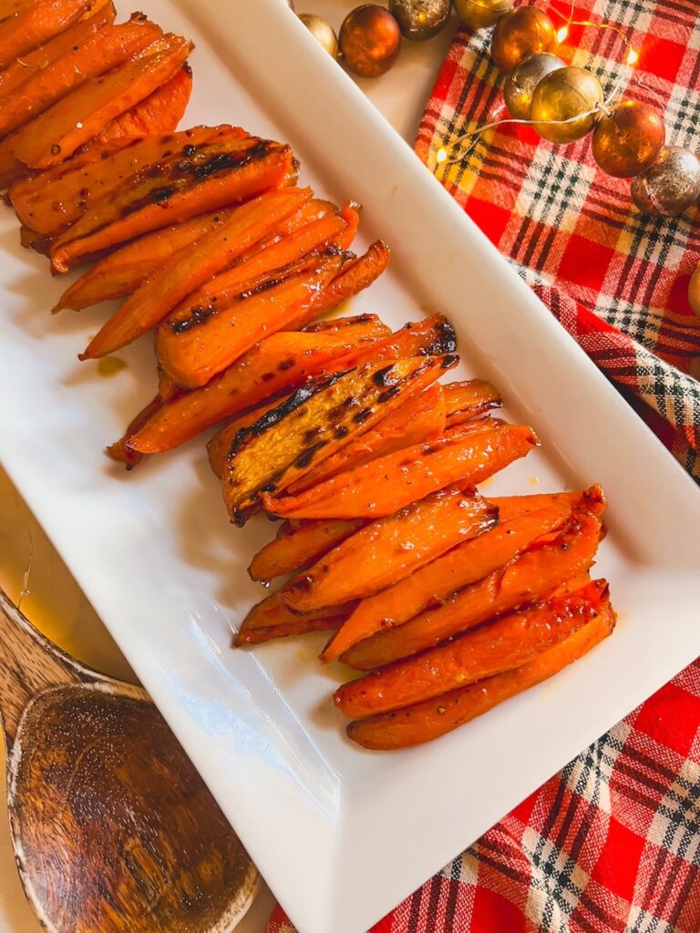 Maple glazed carrots on a white platter with a plaid tablecloth in the background. 