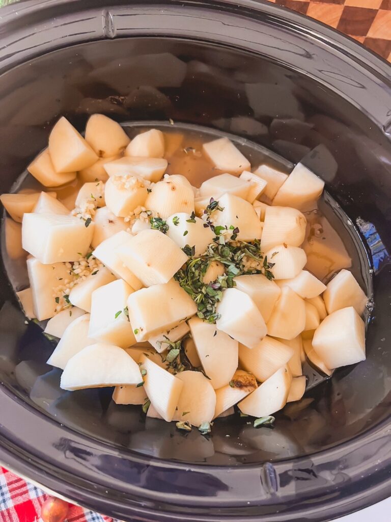 Cubed potatoes, herbs, and broth in a slow cooker. 