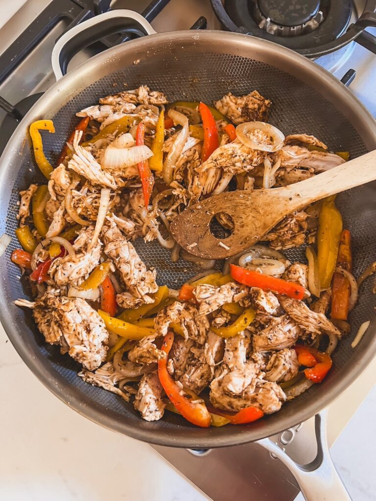 Skillet with peppers, onions, and chicken cooking and a wooden spoon. 