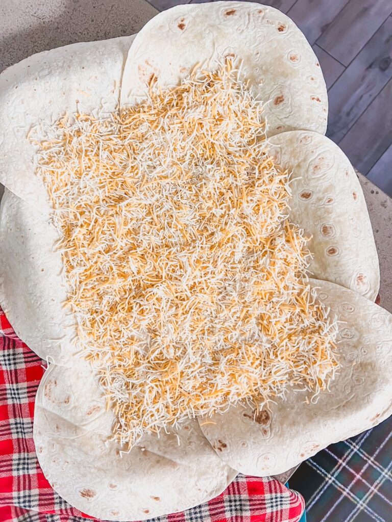 Shredded cheese sprinkled over the flour tortillas on the sheet pan.