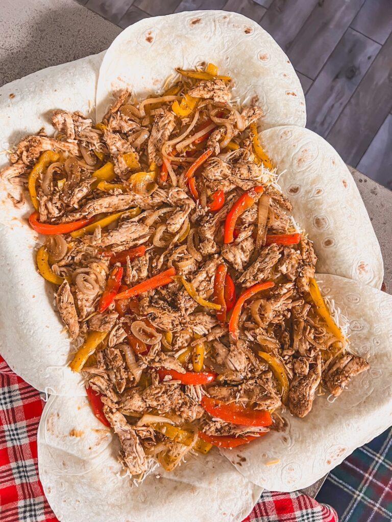 Chicken and peppers spread over the cheese and tortillas in a sheet pan. 