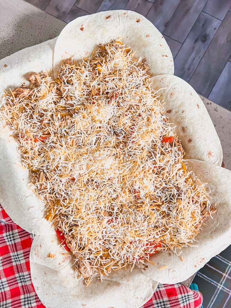 More cheese added on top of the ingredients for chicken fajita quesadillas in a sheet pan.