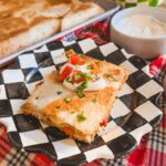 Chicken fajita quesadilla on a checkered plate with the sheetpan quesadilla in the background.