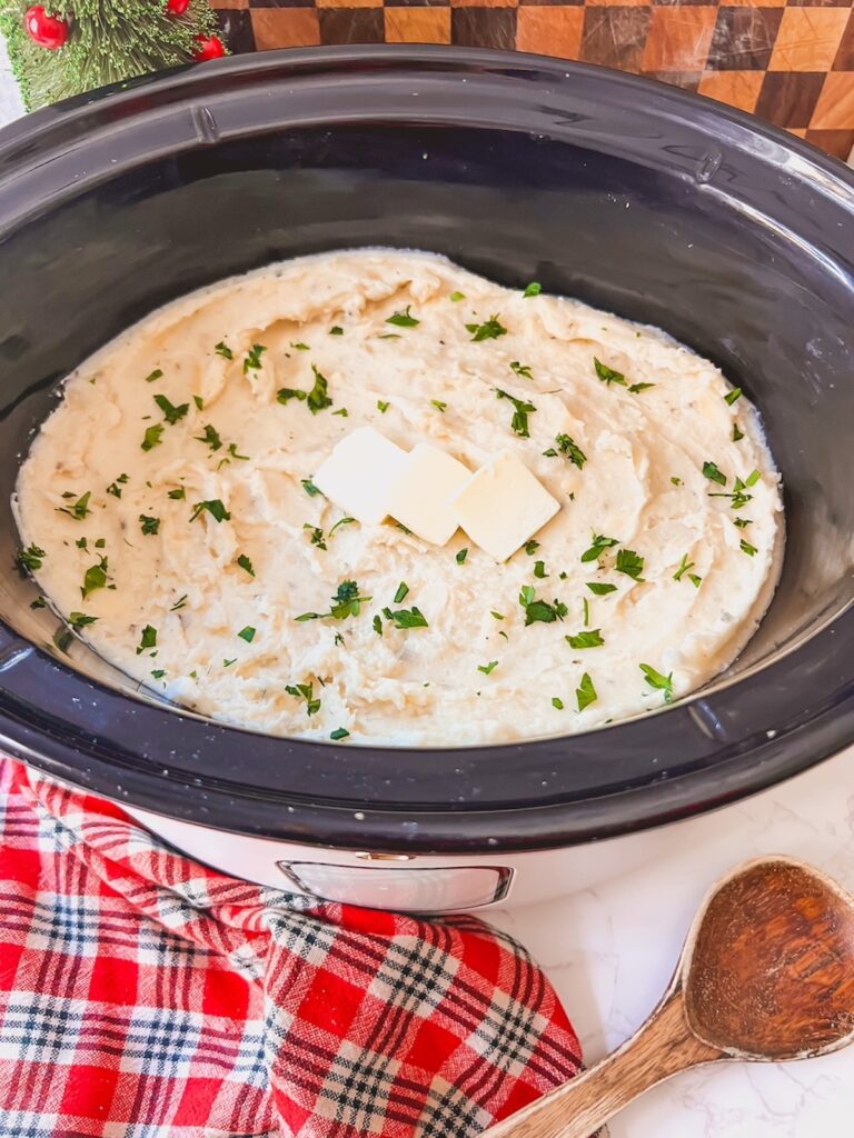 Cheesy garlic mashed potatoes in the slow cooker with butter on top ready to serve. 