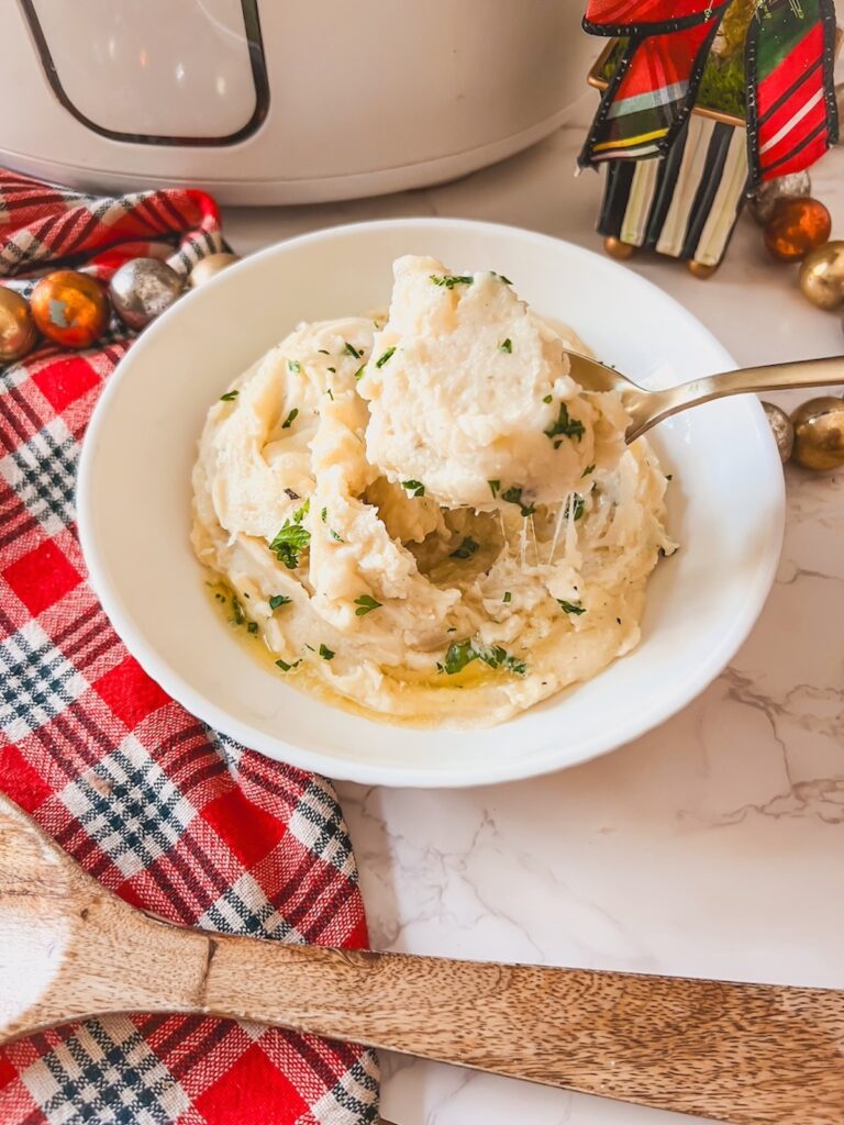Cheesy garlic mashed potatoes in a white bowl with a gold spoon scooping some out. 