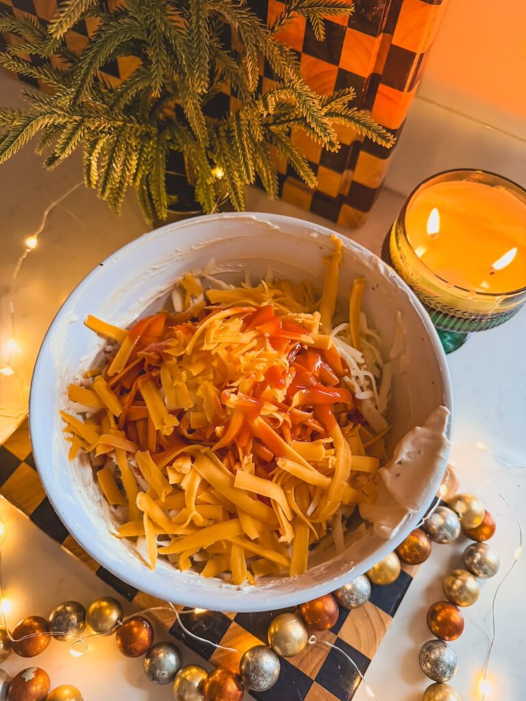 Shredded cheddar cheese on top of the creamy Greek yogurt mixture in a white bowl.