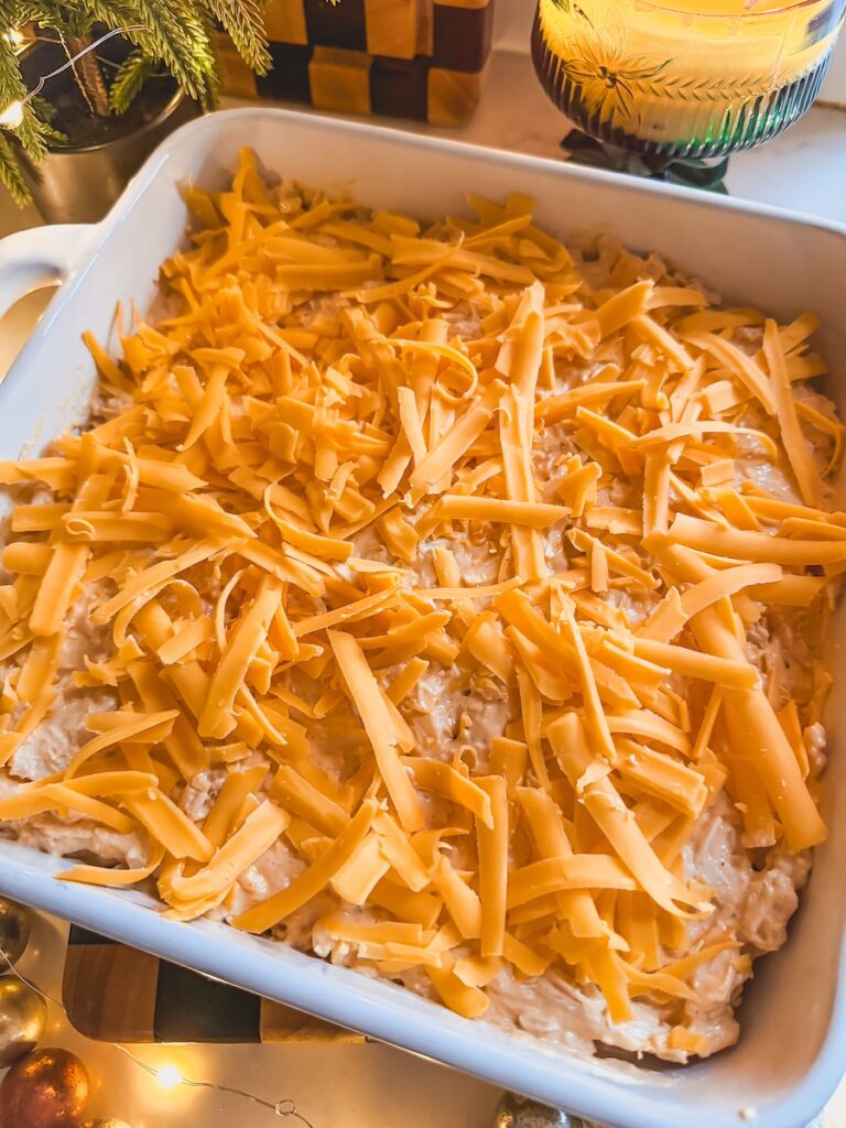 Buffalo chicken dip with shredded cheddar cheese on top in a white baking dish.