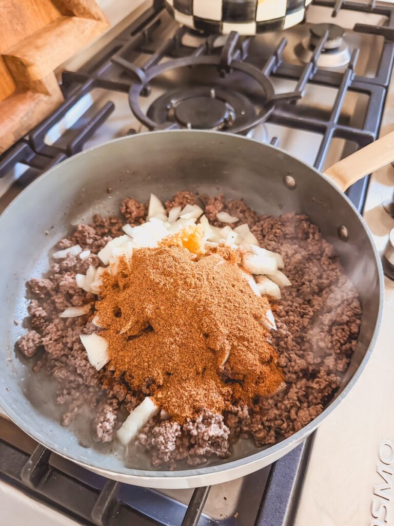 Ground beef cooking in a skillet with onions and spices.