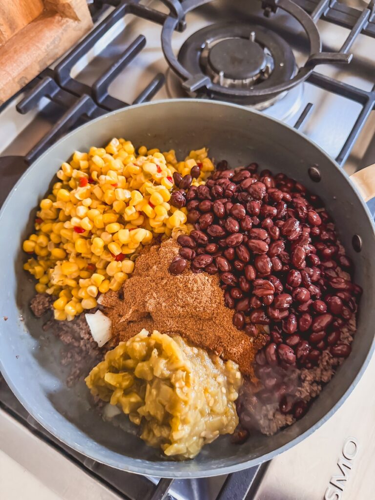 A skillet with ground beef, spices, beans. corn, and green chiles.