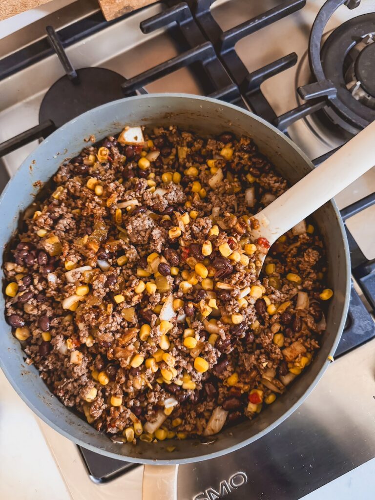 Ground beef with beans, corn, and spices in a skillet with a wooden spoon.
