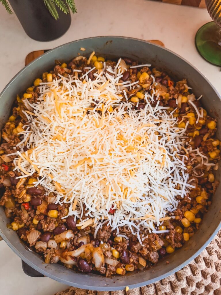 A skillet with ground beef and corn mixture with shredded Mexican cheese on top.